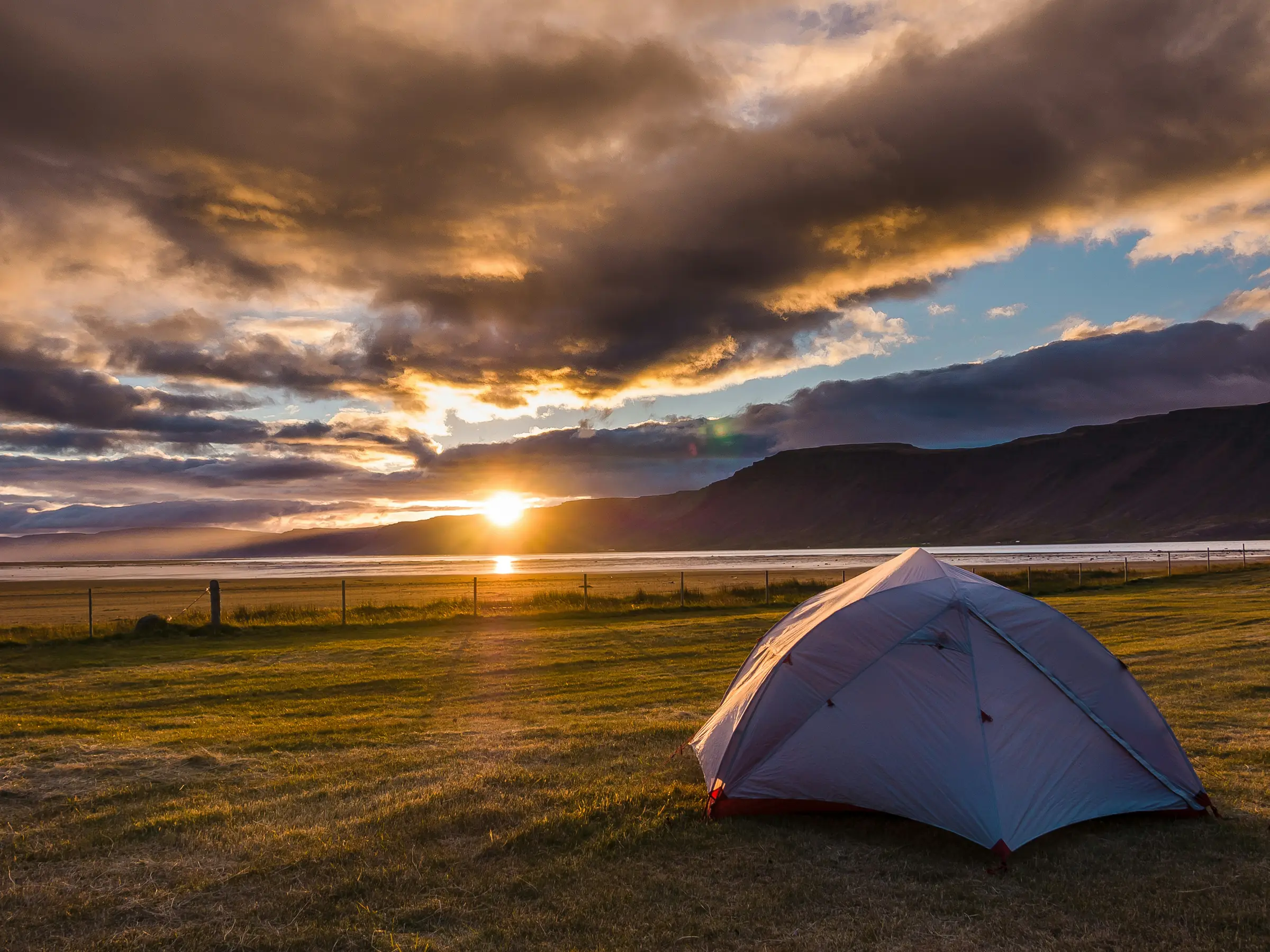 Lakeside tent under dramatic golden-hour clouds