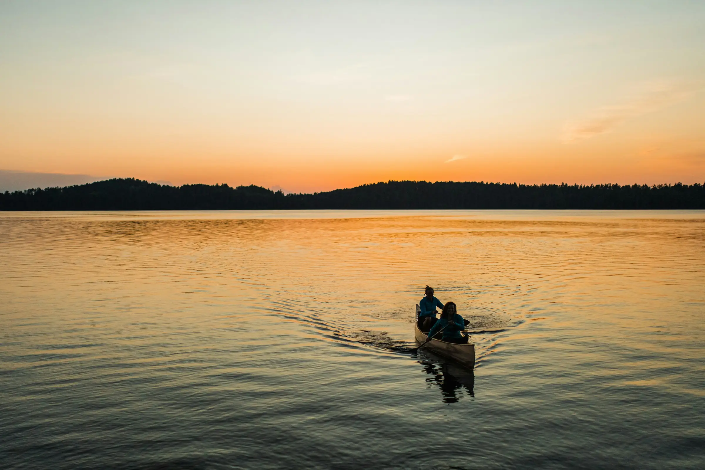 Two campers paddling a canoe at sunset